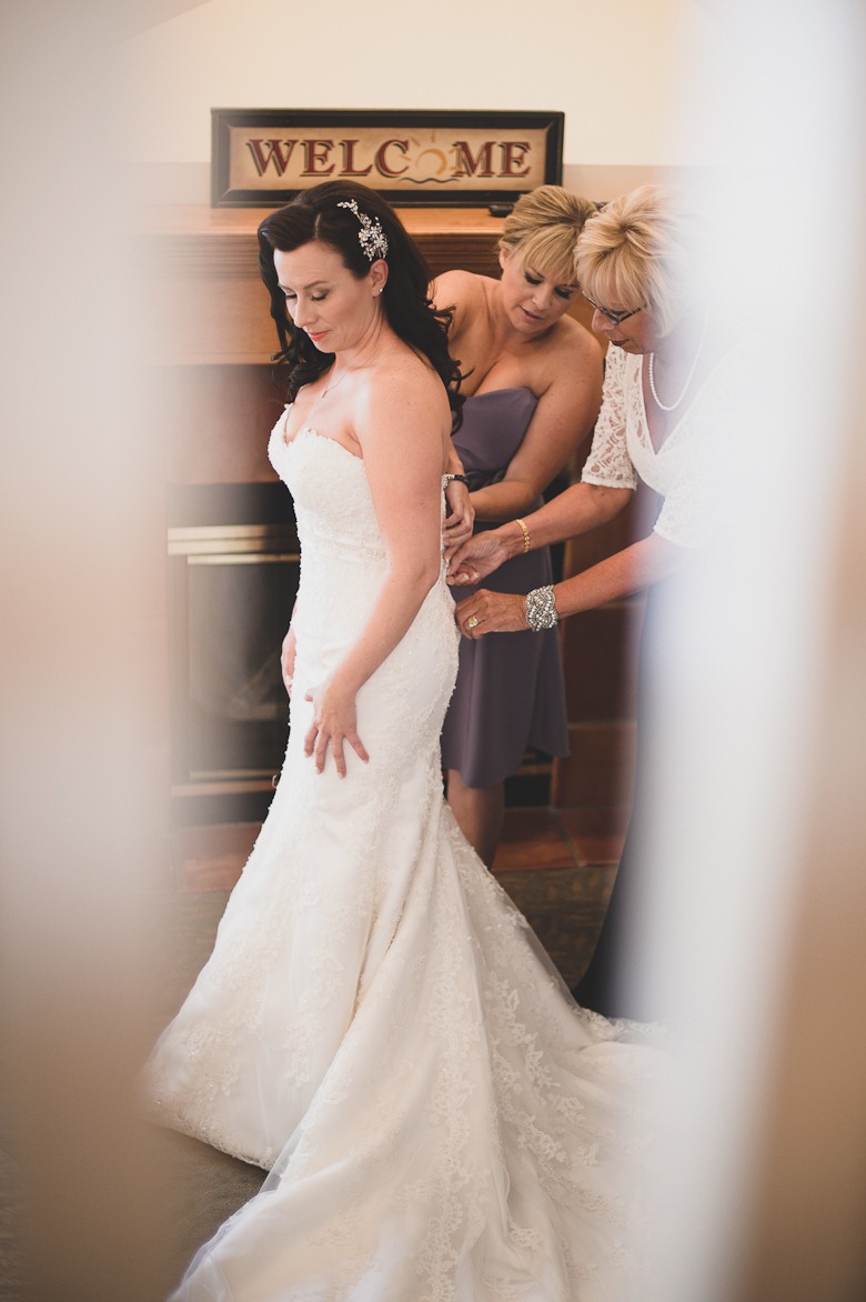 bride puts on dress with mother and sister help at vintage okanagan wedding by nelson, kelowna, bc, wedding photographer electrify photography