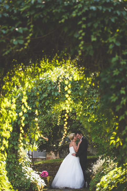 Bride and groom embrace under a archway of greenery in the garden at Blaylock's Mansion, by Nelson BC Kootenay wedding photographer Emilee Zaitsoff of Electrify Photograph
