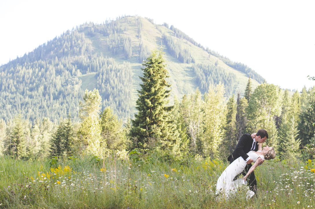 Groom dips his bride for a kiss in blackjack meadow in front of red mountain, rossland, by Nelson BC Kootenay wedding photographer Emilee Zaitsoff of Electrify Photograph
