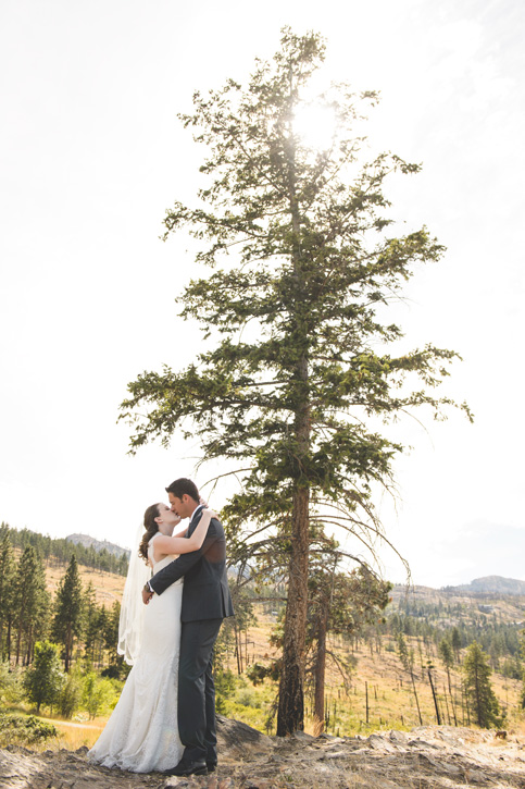 Bride and groom kiss in the hot afternoon sun through trees near Kelowna, BC, Okanagan by Nelson BC Kootenay wedding photographer Emilee Zaitsoff of Electrify Photography